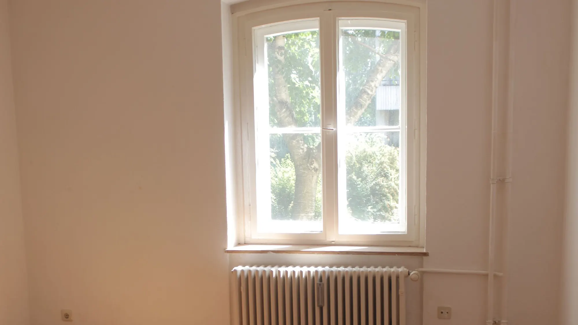 Leerer Wohnraum mit Dielenboden und Heizkörper im Tageslicht. Symbolbild, kein dokumentierter Auftrag.